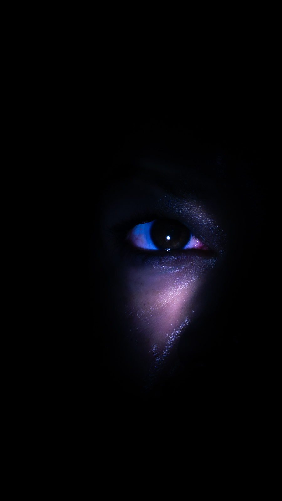 Un ojo iluminado en azul y violeta emerge de la oscuridad, con textura visible en la piel.